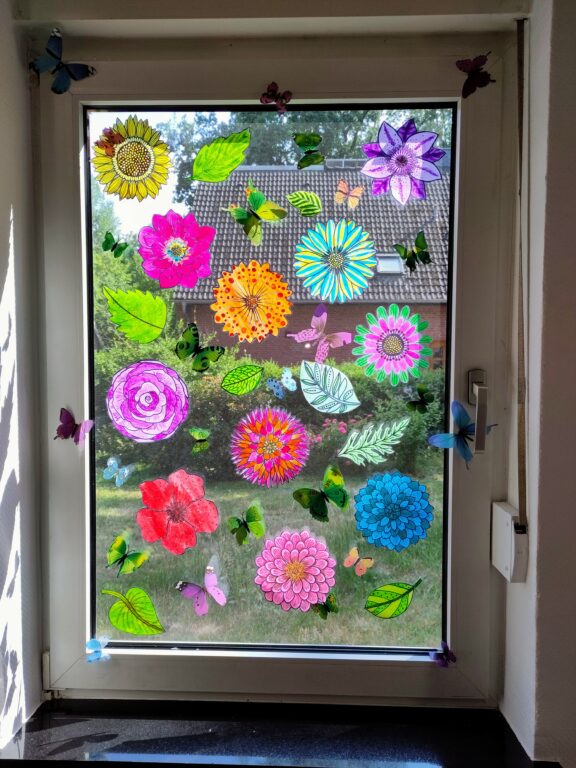 Ein Fenster beklebt mit einer Vielzahl an bunten Papierblüten und Schmetterlingen.