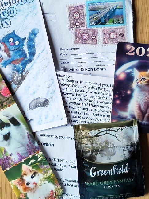 Ein Briefumschlag mit russischen Briefmarken, eine Postkarte mit Katzen, ein Lesezeichen mit Katzen, ein Taschenkalender mit Katzen, ein Brief mit Rezepten und ein Beutel Schwarzer Tee.