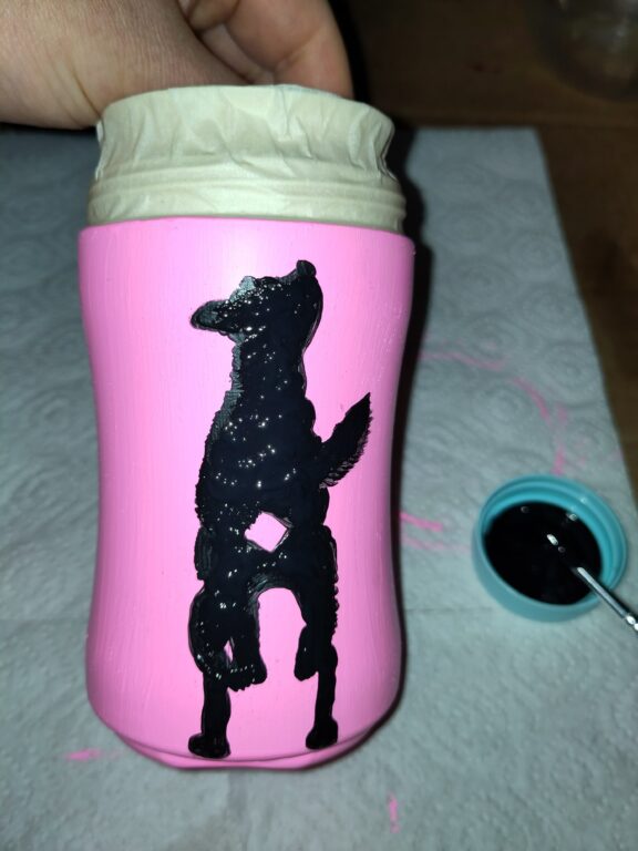 angemalte Kaffeedose in Pink, darauf ein schwarzer gemalter Hund, von hinten zu sehen.