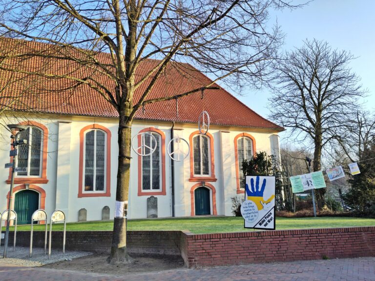 St. Willehadi-Kirche Osterholz-Scharmbeck, im Vordergrund h#ngen Peace-Zeichen und Plakete einer Mahnwache zur Erinnerung an den Krieg in der Ukraine.