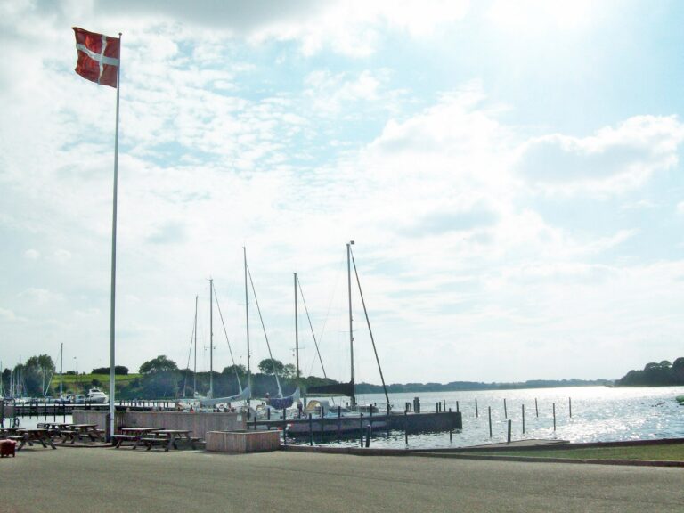 Kleiner Segelboothafen in Dänemark. Zu sehen sind Schiffe und eine gehisste Dänemarkflagge.